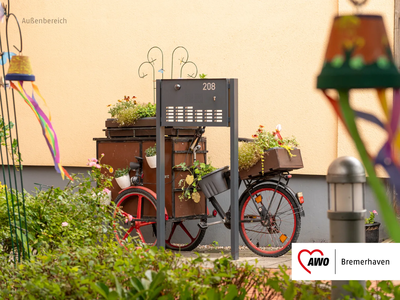 Hinterer Eingangsbereich Bürger 208 | © AWO Bremerhaven Ein dekoratives Fahrrad mit mehreren Blumenkästen steht vor einem Briefkasten | © AWO Bremerhaven